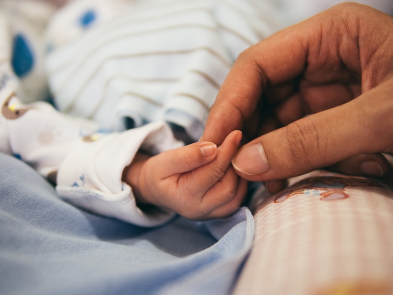 An adult hand holding a baby finger